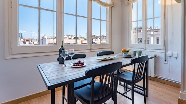 Un comedor con una mesa de madera, sillas negras y vistas de la ciudad a través de grandes ventanales.