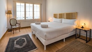 Un dormitorio con una cama grande, una silla, una lámpara y una ventana.
