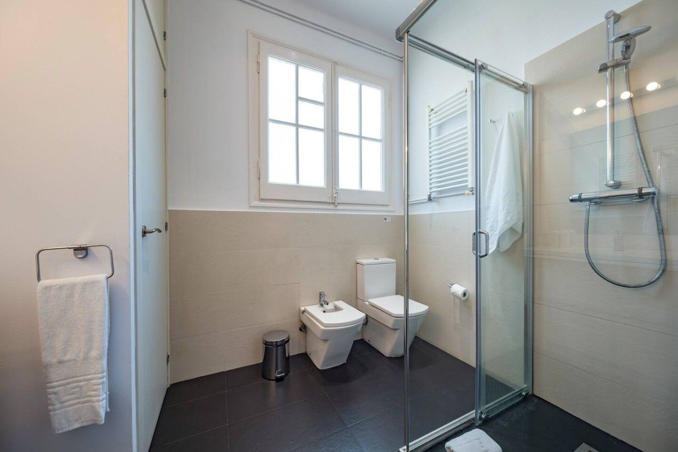 A modern bathroom with a glass shower enclosure, a toilet, and a bidet.