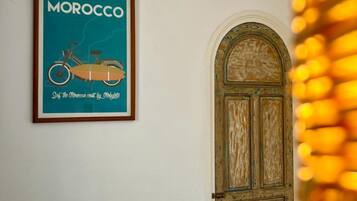 A bedroom with a bed, a framed poster of Morocco, a wooden door, and a wall socket.