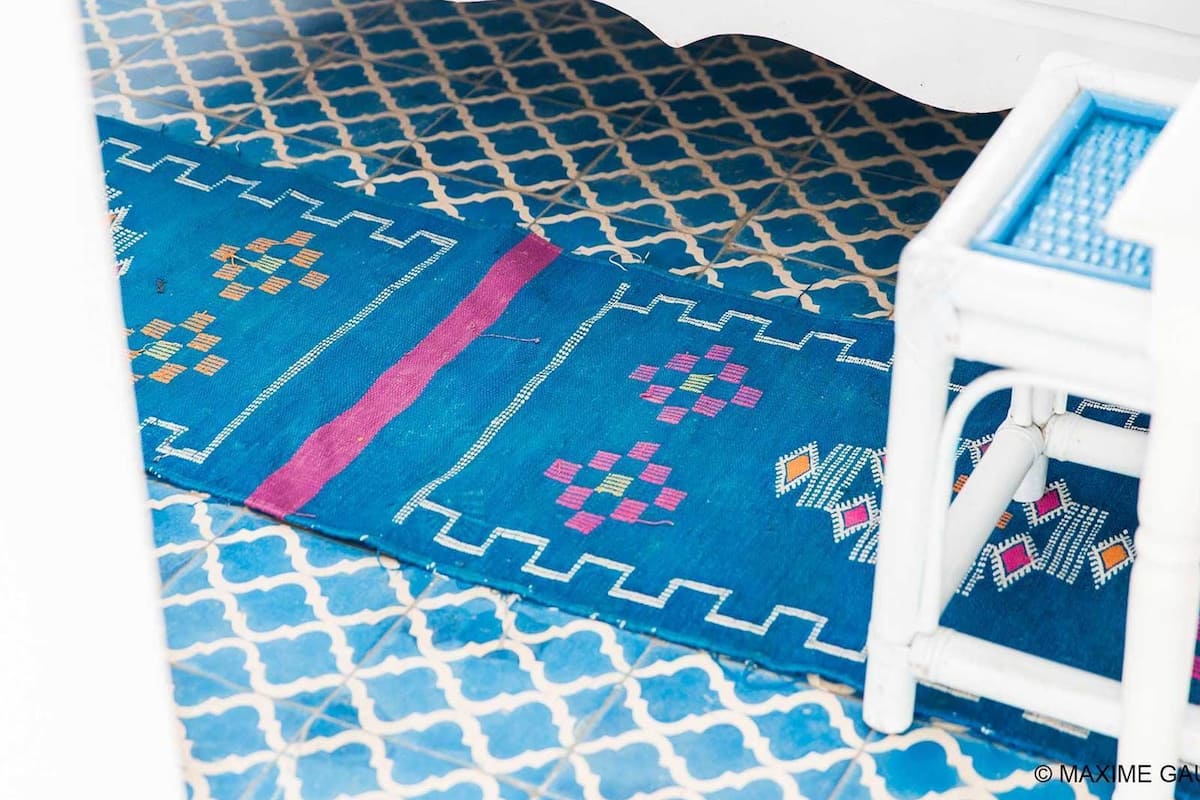 A patterned blue carpet with geometric designs and a white chair with a blue cushion.
