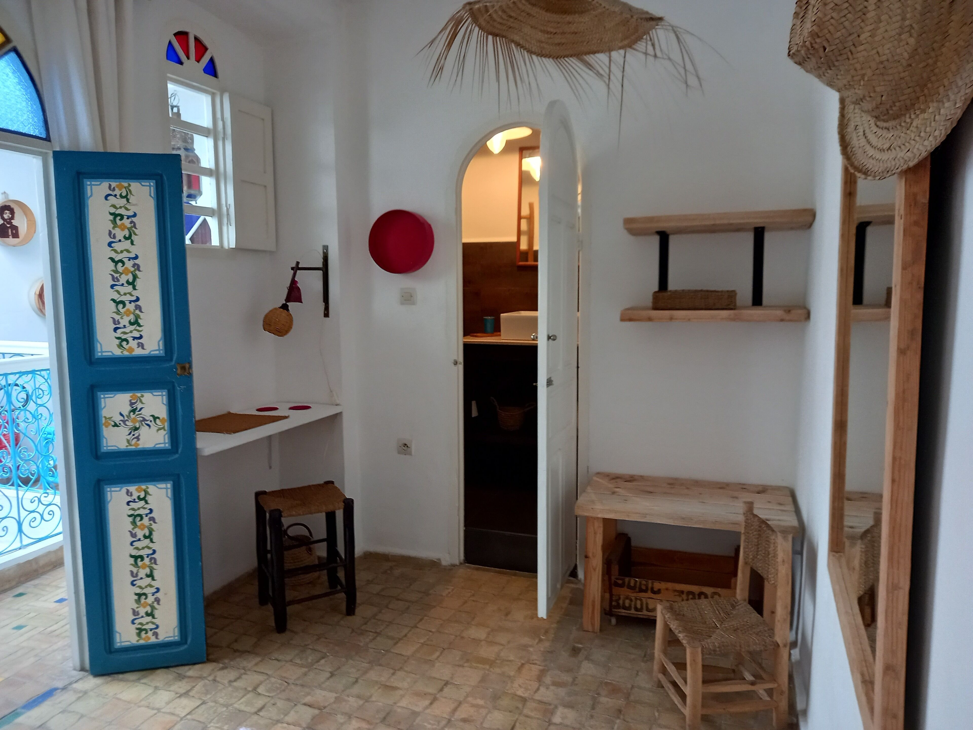 A room with a blue door, a small stool, a wooden table, and shelves.