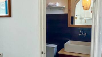 A bathroom with a white sink, a mirror, and a toilet. There is a towel rack with towels and a roll of toilet paper.