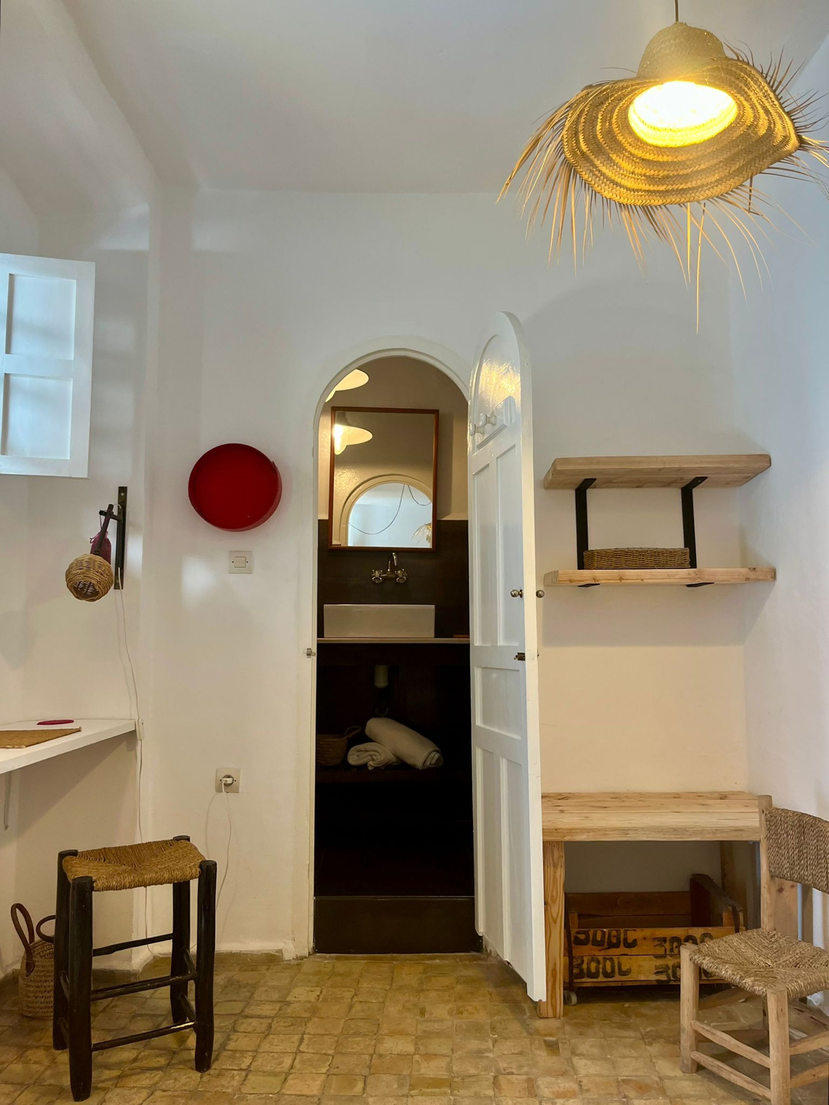 A hallway with a woven light fixture, a red circular object on the wall, and a wooden bench.