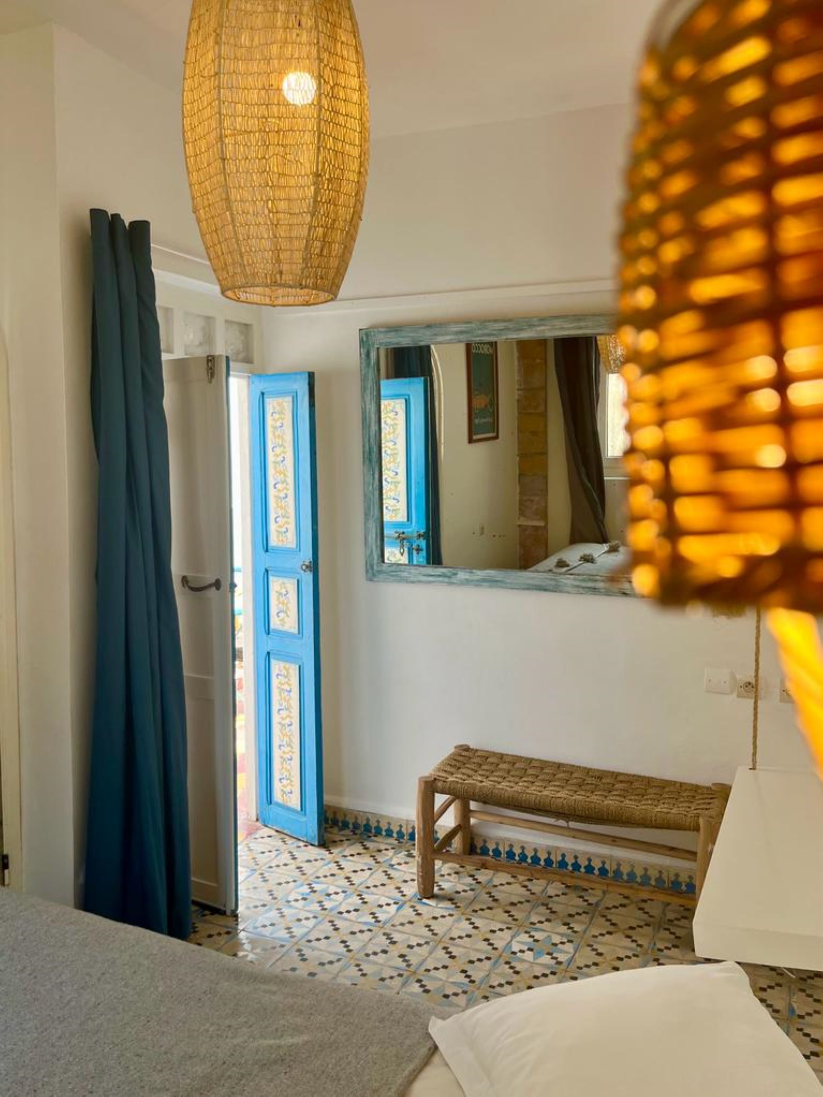 A room with a bed, a bench, a mirror, and a door.