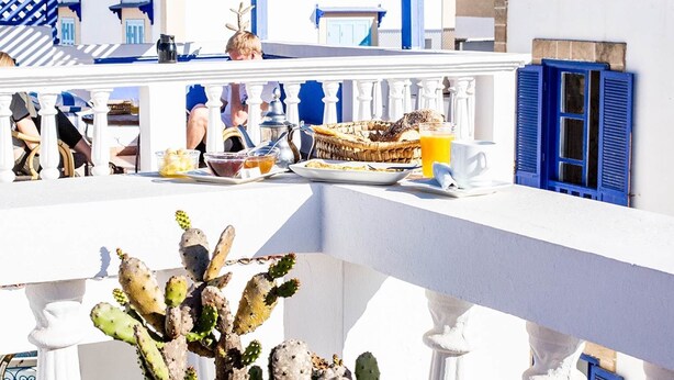 A balcony with a breakfast setup including a basket of bread, a cup of coffee, and a glass of orange juice. - Hotel Emeraude Essaouira (Essaouira)