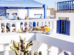 A balcony with a breakfast setup including a basket of bread, a cup of coffee, and a glass of orange juice. - Hotel Emeraude Essaouira (Essaouira)
