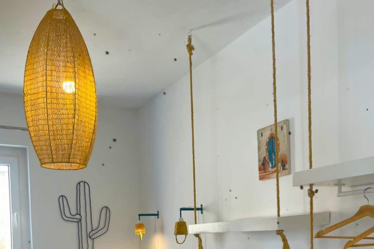 A bedroom with a bed, a hanging light fixture, a cactus wall decoration, and a shelf with a picture.