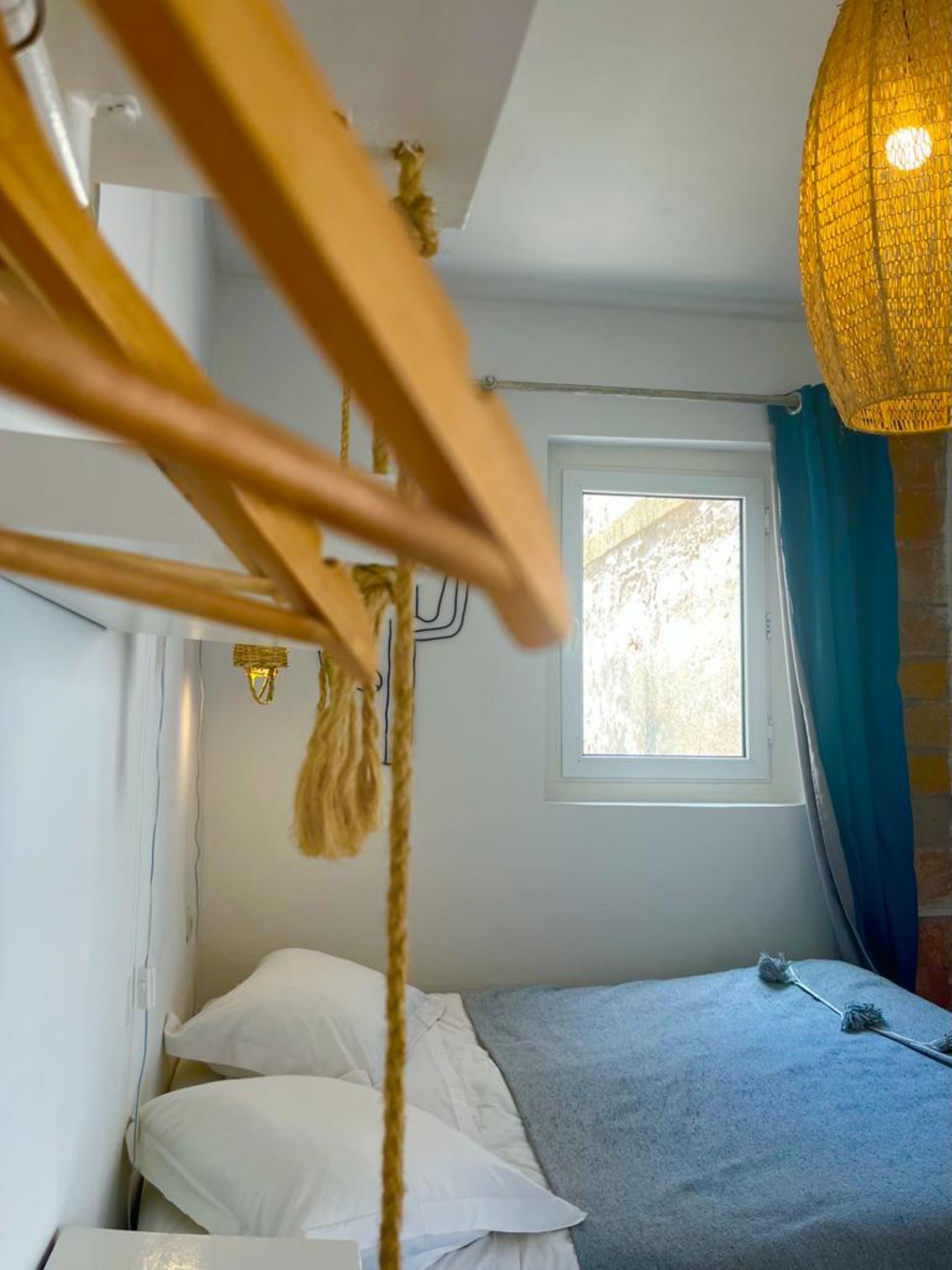 Ein Zimmer mit einem Bett, einem Fenster und einer Pendelleuchte.