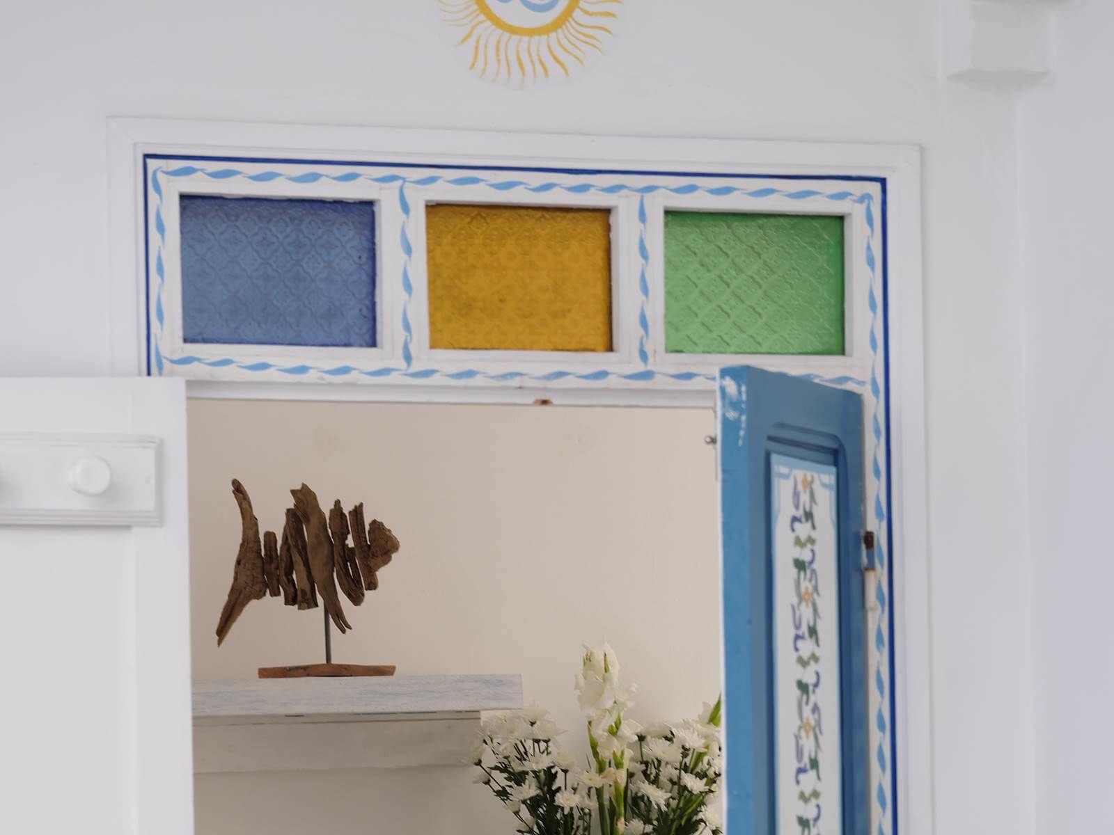 A room with a white door, a blue-framed window, and a wall-mounted decorative piece.