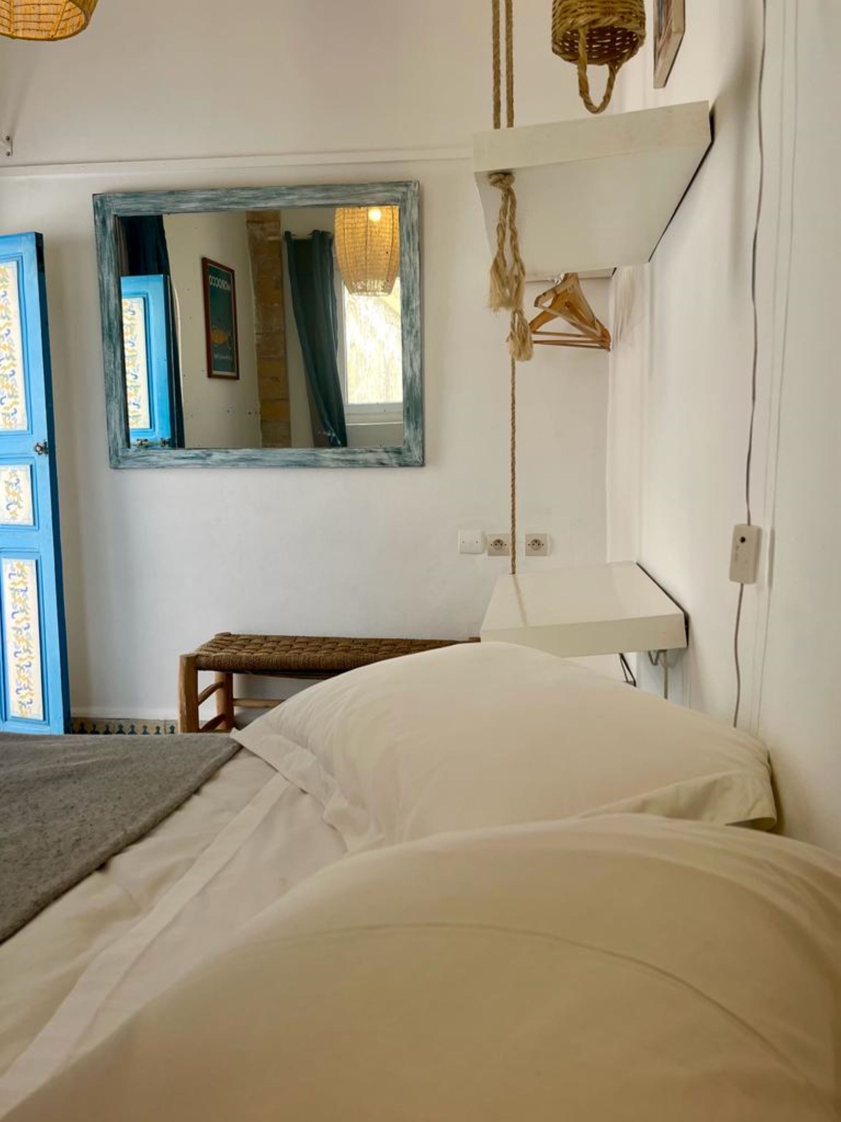 A bedroom with a bed, a small table, a hanging basket, and a mirror on the wall.
