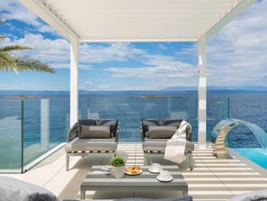 A balcony with two chairs, a table with a plant and a plate of food, and a glass railing overlooking the sea. - Vacation home Palma by Interhome (Korcula/Prigradica)