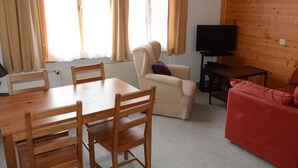 Een woonkamer met een houten tafel, stoelen, een bank, een televisietoestel en een raam met gordijnen.