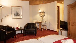 A hotel room with a large bed, two chairs, a desk with a lamp, a television, and framed pictures on the walls. - Chalet Abendrot apARTments by Interhome (Grindelwald)