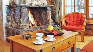 A cozy room with a stone fireplace, a wooden table with cups and a bowl, and a red chair. - Näätämö by Interhome (Asikkala)