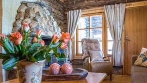 A cozy room with a wooden floor, a stone wall, a fireplace, a chair, and a table with a vase of flowers. - Näätämö by Interhome (Asikkala)