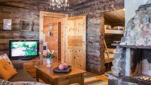 A cozy log cabin interior with a stone fireplace, wooden walls, a television, and a comfortable seating area. - Näätämö by Interhome (Asikkala)