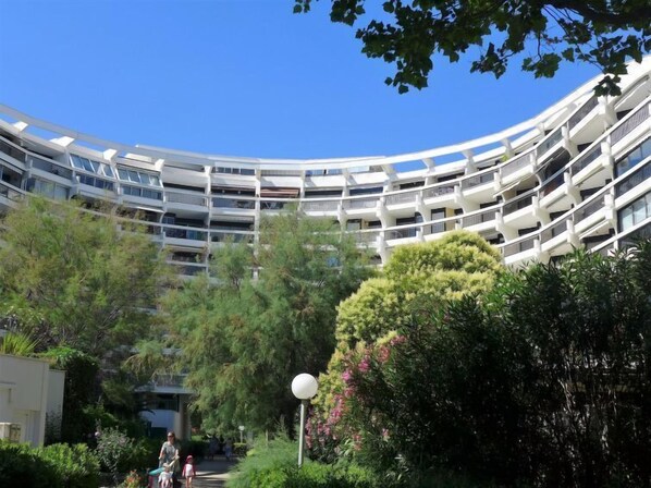 A modern, multi-story building with a curved facade, surrounded by lush greenery and a clear blue sky.