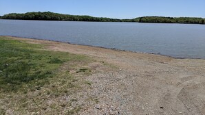 A calm lake with a grassy shore and a forested hill in the background. - Welcome to Pearl Haven - a 500 sf gem! Hosting both Long and Short-term rentals! (Camden)