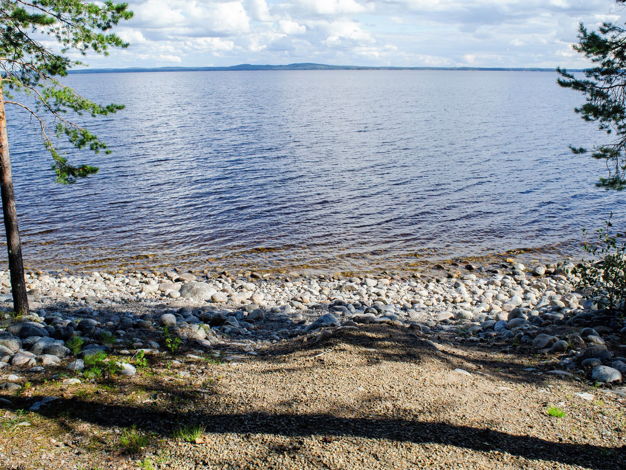 A rocky shoreline with a view of a calm body of water and distant land.