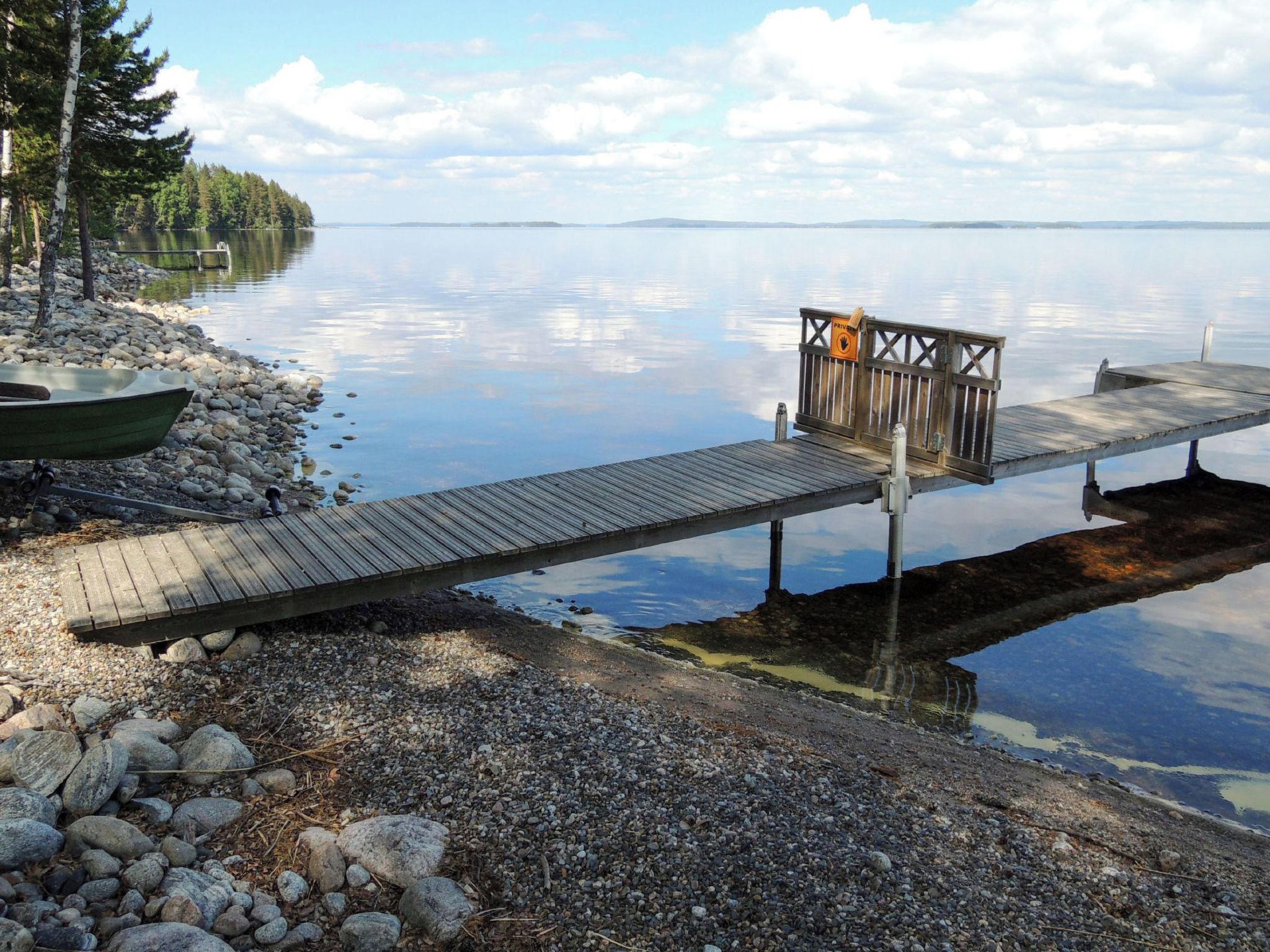 A wooden dock extending into calm water with a rocky shore and a boat on the left.