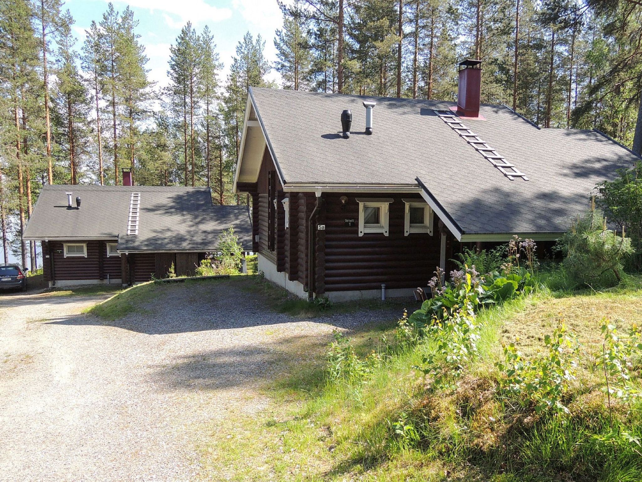 A cabin with a chimney, a ladder, and a gravel driveway.