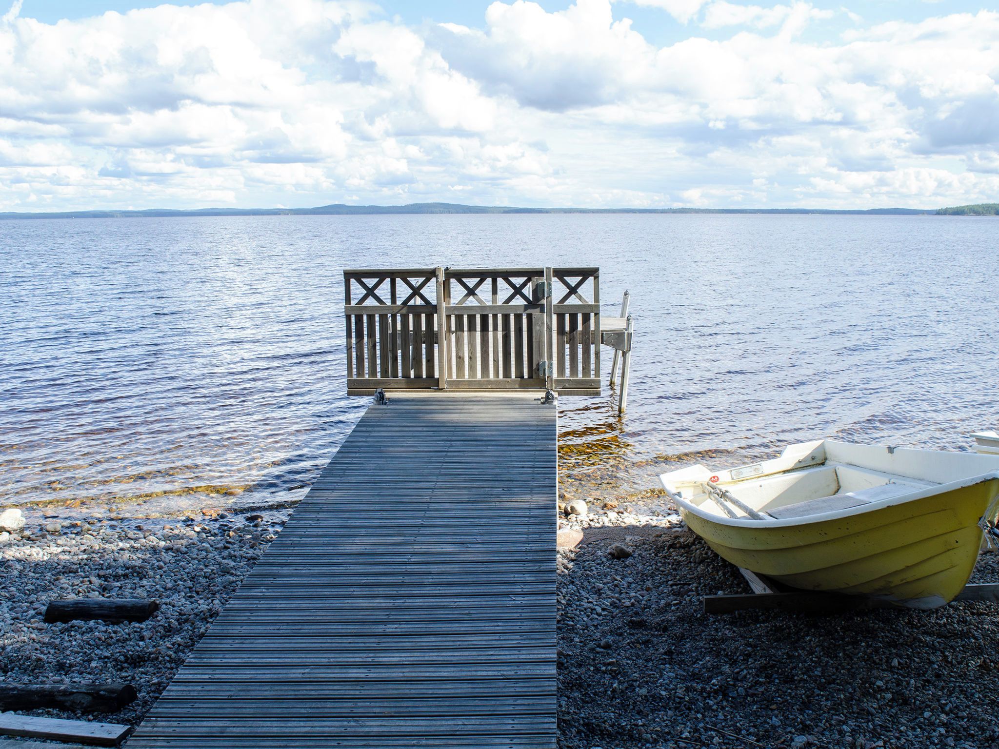 A wooden dock leading to a dock gate with a boat on the shore.