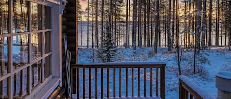 A wooden deck leading to a cabin with a view of a snowy forest.