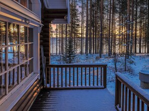 A wooden deck leading to a cabin with a view of a snowy forest.
