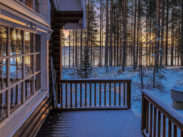 A wooden deck leading to a cabin with a view of a snowy forest.