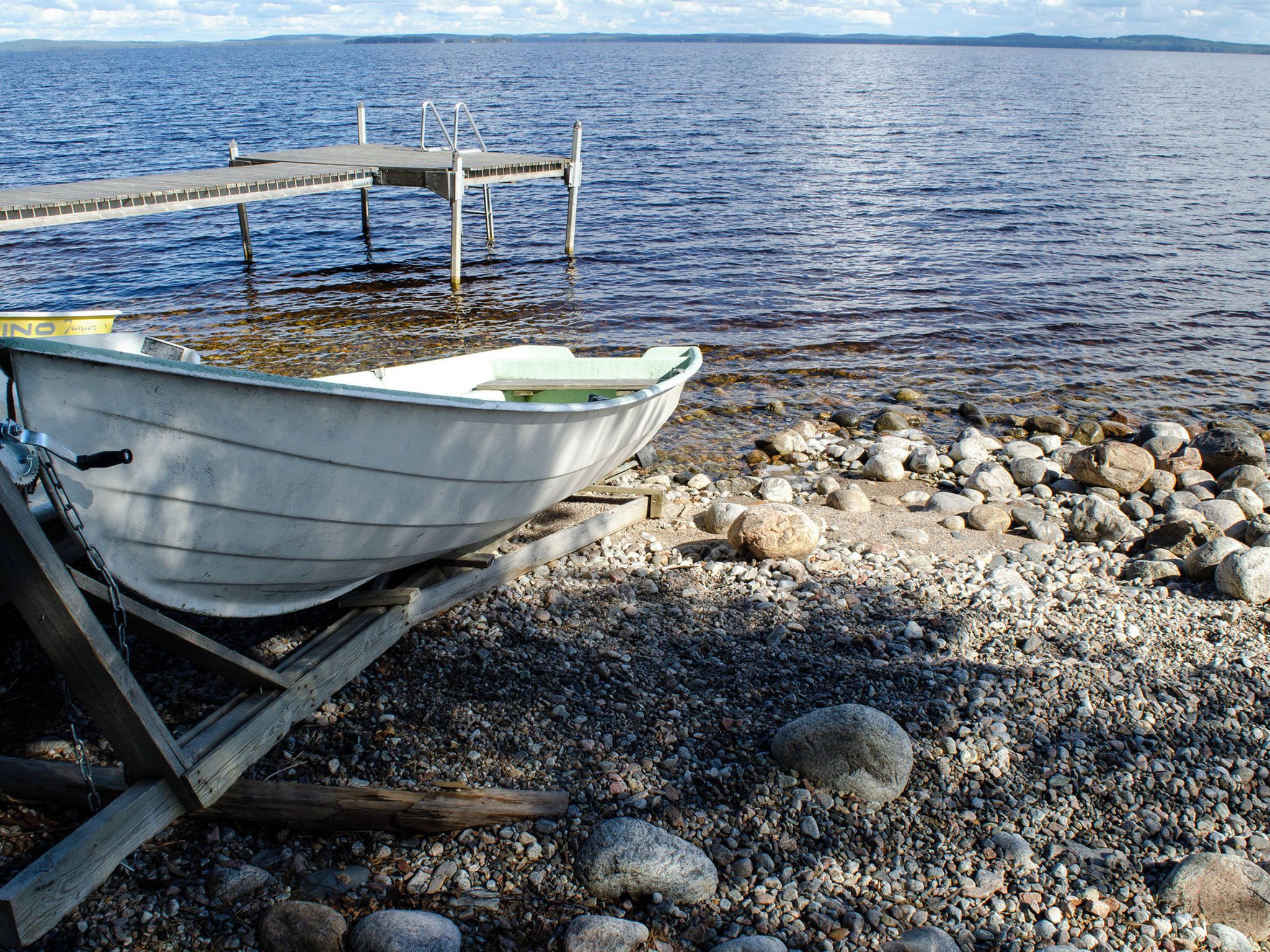 A boat tied to a wooden dock with a rocky shore in the background.