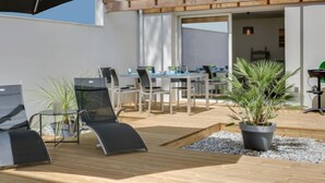 Un'area esterna con tavoli e sedie di legno, un ombrellone nero e piante in vaso.