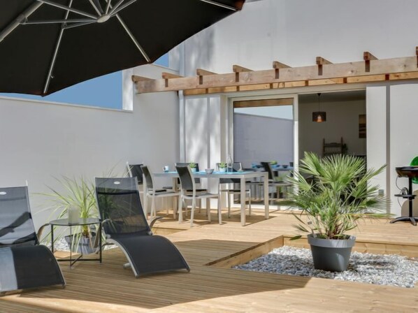 An outdoor seating area with wooden tables and chairs, a black umbrella, and potted plants. - Les Patios de Flore by Interhome (Mimizan)