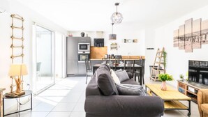 Un soggiorno moderno con divano, tavolino e televisione. Si intravede una cucina sullo sfondo con un'area pranzo.