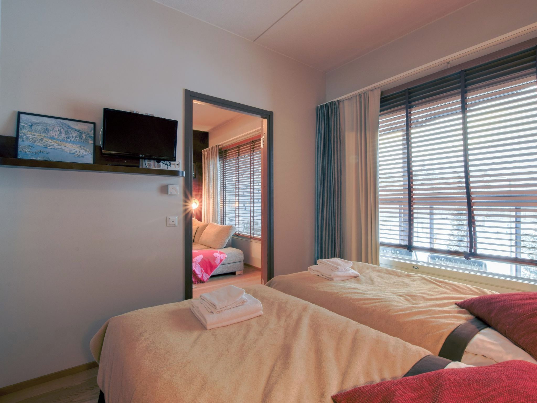 Ett hotellrum med två sängar, en tv som är monterad på väggen och ett fönster med persienner.