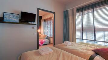 Ett hotellrum med två sängar, en tv som är monterad på väggen och ett fönster med persienner.