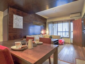 Een moderne woonkamer met een houten eettafel, een zithoek en een groot raam met zonwering.