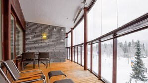 A wooden deck with wicker chairs and a table, large windows with a snowy view, and a stone wall. - Tahko spa junior suite orange b6 by Interhome (Nilsiä)