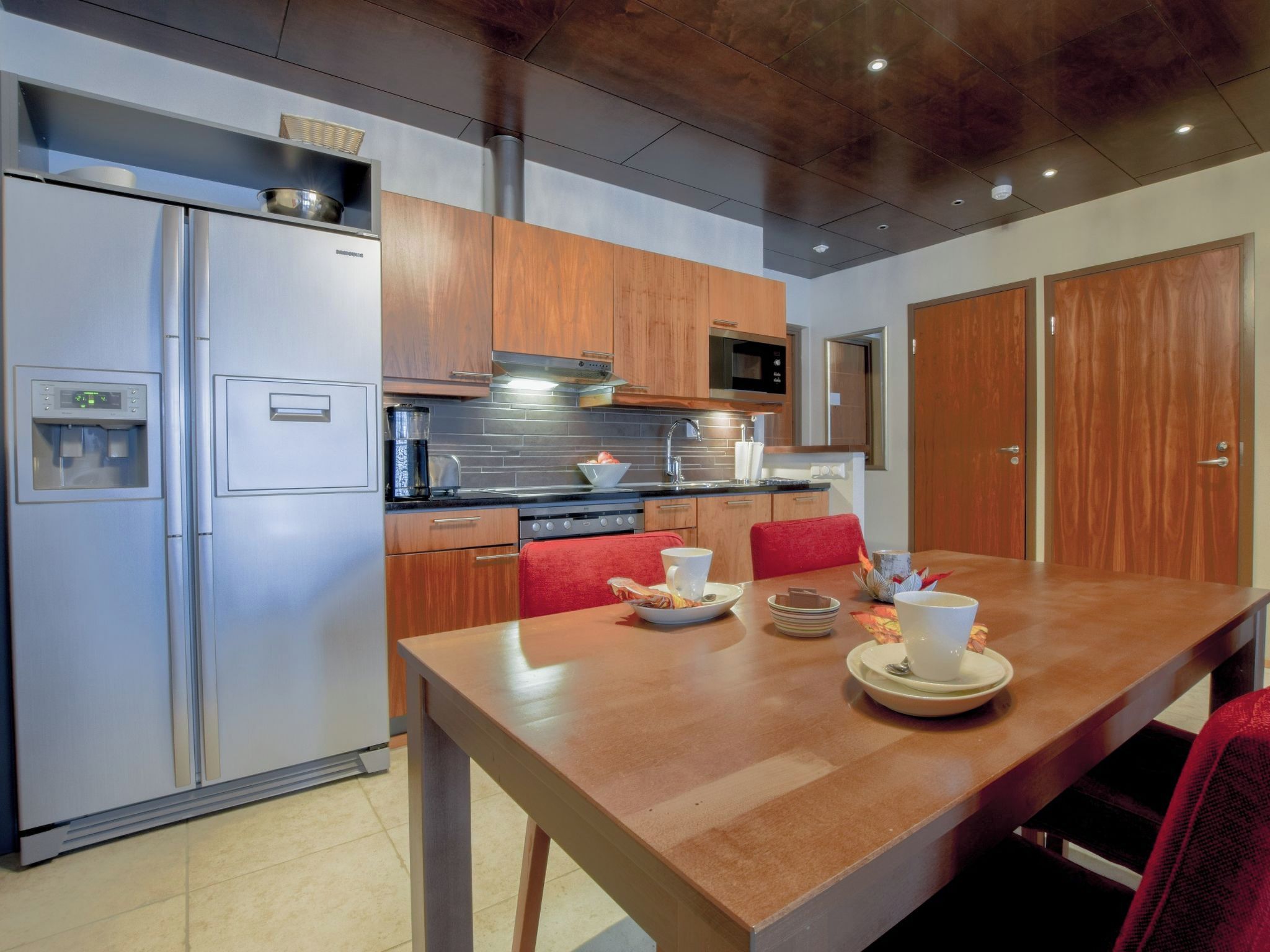 A modern kitchen with stainless steel appliances, wooden cabinets, and a dining table set for two.