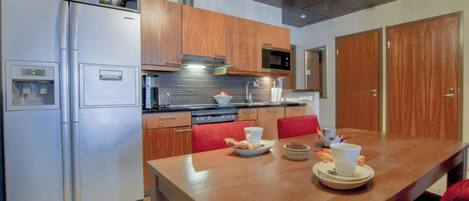 A modern kitchen with stainless steel appliances, wooden cabinets, and a dining table set for two.