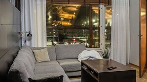 A modern living room with a grey sofa, a coffee table, and a view of a street scene through large windows. - Tahko spa junior suite orange b6 by Interhome (Nilsiä)
