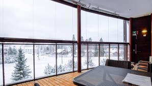 A wooden deck with a table and chairs, large windows with a view of a snowy landscape, and a door with a sign. - Tahko spa junior suite orange b6 by Interhome (Nilsiä)