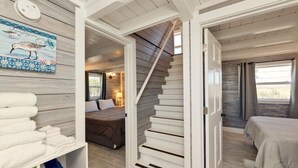 A staircase leading to a bedroom with a bed and a nightstand, a shelf with folded towels, and a wall with a decorative piece.