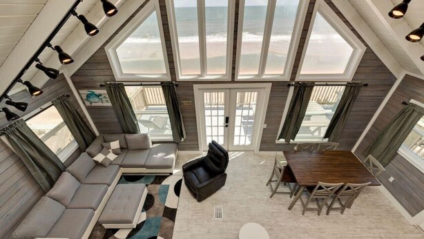 A spacious living area with a large window overlooking the beach, a wooden dining table, and a comfortable seating arrangement.