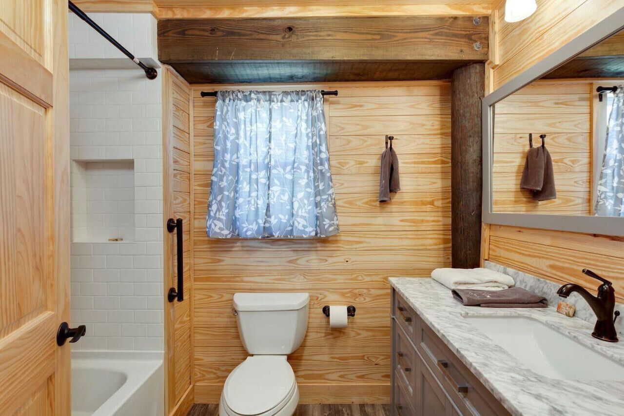 A compact bathroom with a wooden interior, a toilet, a shower, and a sink with a marble countertop.