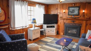 Ein gemütliches Wohnzimmer mit Holzwänden, einem Fernseher, einem Kamin und maritime Möbeln.