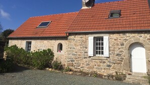 A stone building with a red-tiled roof, a small window, and a white door. - THE HOUSE OF LAVOIR. (PLOUGUIEL)