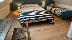 A cozy bedroom with a sloped ceiling, a bed with striped bedding, a bedside table with a lamp, and a hanging light fixture. - THE HOUSE OF LAVOIR. (PLOUGUIEL)