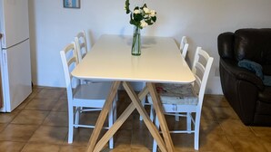 A dining area with a white table and chairs, a vase with flowers, a clock on the wall, and a brown leather couch. - THE HOUSE OF LAVOIR. (PLOUGUIEL)