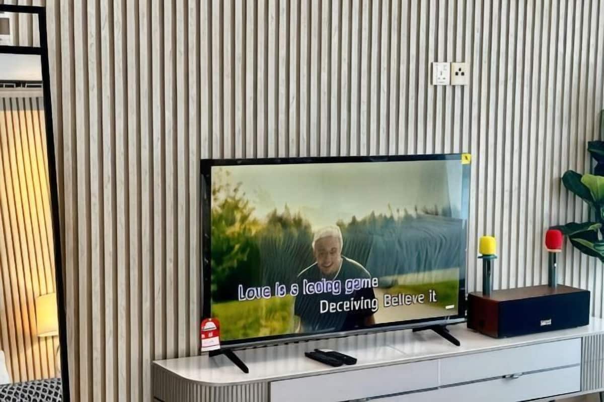A flat-screen TV mounted on a wall with a striped pattern, a remote control, and a decorative object on the stand.